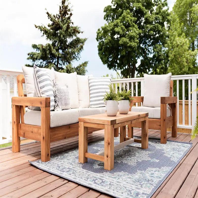 Handcrafted wooden outdoor patio furniture set by StandCraft Canada, including a sofa, armchair, and coffee table with cushions, shown on a deck.